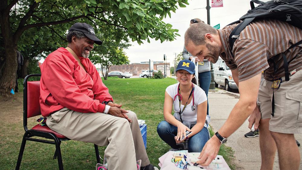Three people gathered outside, smiling and looking down at a small supply of items on the ground.